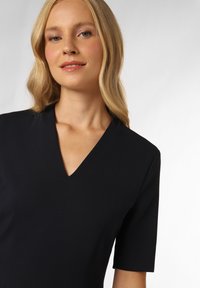 Schwarzes Kleid mit V-Ausschnitt und kurzen Ärmeln, aus einem glatten Stoff gefertigt. Einfaches Design ohne sichtbare Muster oder Verzierungen.