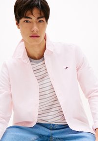 Lichtroze overhemd met een open kraag, gelaagd over een grijs-wit gestreept T-shirt, gecombineerd met blauwe denim jeans.