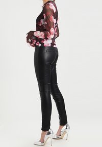 Black faux leather pants with a smooth texture, paired with a sheer black floral top featuring pink and red rose patterns. Silver heels accentuate the look.