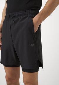 Pantalones cortos deportivos negros con cinturilla elástica y cordón, que cuentan con bolsillos laterales y un pantalón interior ajustado para mayor comodidad.