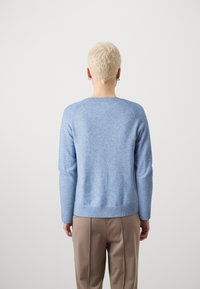 Maglione lavorato a maglia blu chiaro con maniche lunghe, orlo e polsini a coste, scollatura rotonda e un taglio morbido, abbinato a pantaloni beige.