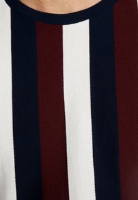 Stribet T-shirt i mørkerød, navy og hvid. Har en ribbet rund hals og tekstureret stof med lodrette striber i forskellige bredder.