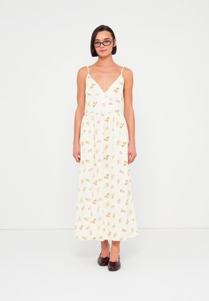 Maxi sukienka w kremowym kolorze z kwiatowym wzorem w różowym i pomarańczowym kolorze, dekolt w serek, cienkie ramiączka i marszczona talia; noszona z ciemnymi butami.