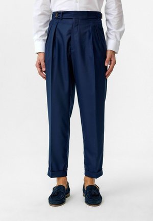 Donkerblauwe geplooide broeken met een getailleerde pasvorm, voorzien van een hoge taille, riemlussen en twee knopen bij de taille. Textuurstof met manchetten.