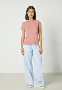 Różowy t-shirt z krótkim rękawem wykonany z miękkiego materiału, zestawiony z jasnoniebieskimi spodniami o szerokich nogawkach z delikatnym paskowanym wzorem.