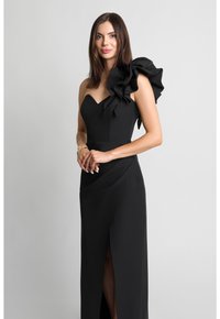 Czarna wieczorowa sukienka z dekoltem w kształcie serca i dużym falbaną na jednym ramieniu. Posiada dopasowaną górę i rozcięcie do uda w spódnicy.
