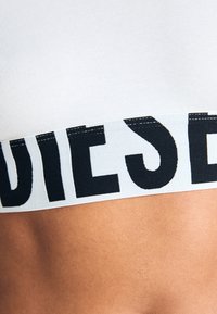 Witte katoenen stretchstof met een brede elastische tailleband waarop "DIESEL" in vetgedrukte zwarte letters staat. Gladde textuur, strakke pasvorm.