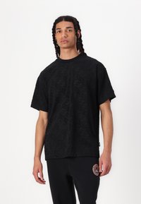 Tricou negru cu mâneci scurte, cu un model subtil, decolteu rotund și croială lejeră, asortat cu pantaloni negri care au un logo colorat.