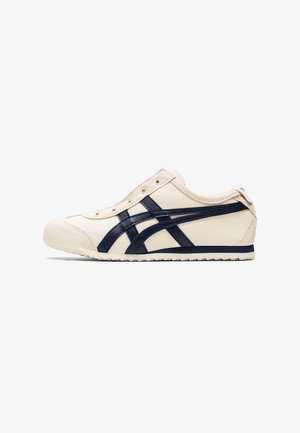 Kermanvalkoinen kangaskenkiä, jossa tummansinisiä raitoja ja kuminen pohja, nähtynä sivulta ilman nauhoja, valkoisella taustalla.