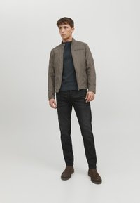 Grå ruskindsjakke med en opretstående krave, parret med en marineblå sweater og sorte jeans. Brune ankelstøvler tilføjer kontrast til outfittet.