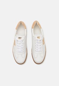 Baskets en cuir blanc avec des accents beige clair, lacets plats, côtés texturés et semelle en caoutchouc. Présente le logo de la marque en doré sur le côté.