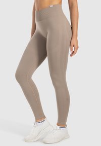 Beige high-waisted leggings gemaakt van rekbare, gestructureerde stof met subtiele naaddetails, gecombineerd met witte sportschoenen.