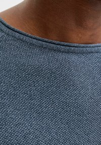 Strikket mørkegrå genser med rund hals og et strukturert mønster, med jevn og glatt søm langs kragen.