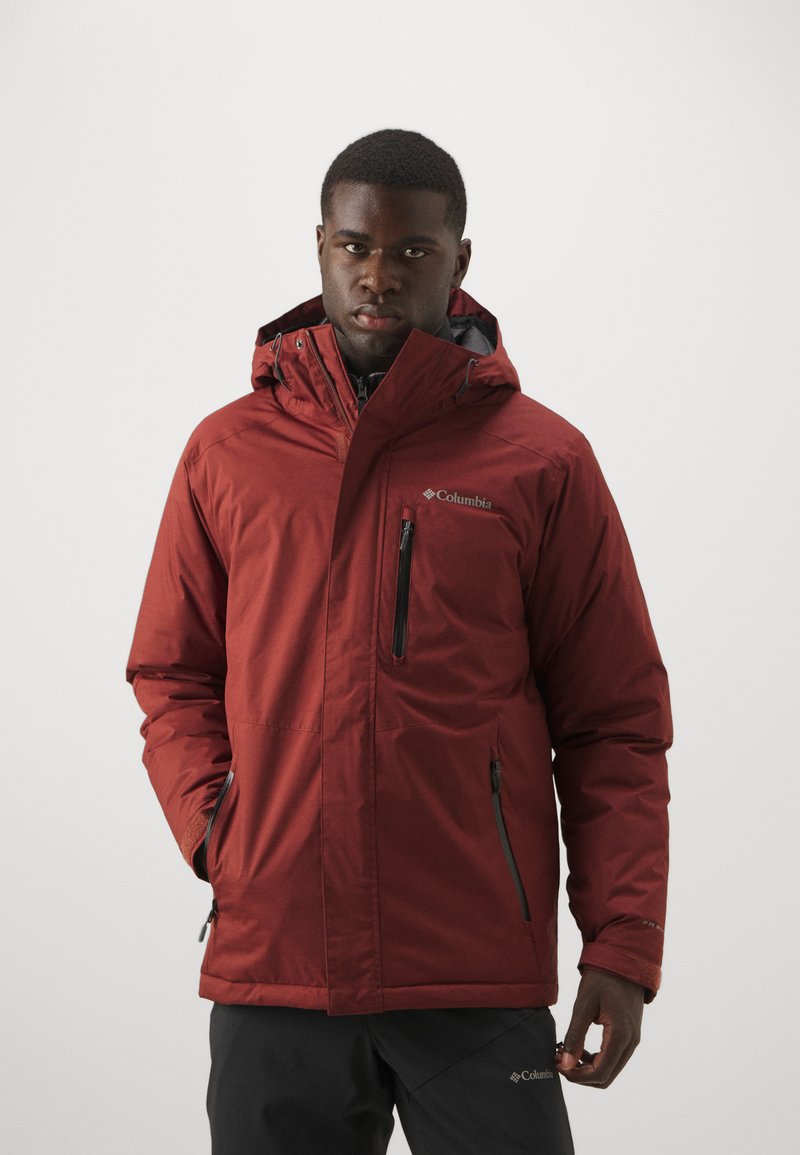 Chaqueta impermeable roja con capucha, que cuenta con un bolsillo en el pecho con cremallera y bolsillos laterales, hecha de un suave tejido sintético con un acabado mate.