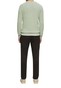 Un pull vert clair à col rond et à manches longues, associé à un pantalon noir. La tenue présente une coupe décontractée et des poignets côtelés.