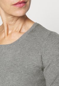 Grau gerippter Pullover mit Rundhalsausschnitt. Der Stoff wirkt weich und strukturiert und hat eine körpernahe Passform. Subtile feine Details sind sichtbar.