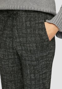 Zwarte en grijze gestreepte broek met een elastische tailleband en trekkoord. Voorzien van voorzakken en een gestructureerde stof.