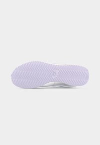 Balta kedas zolīte ar lavandas krāsas zigzagveida rakstu un centrālo Nike logotipu uz vienkārša gaiša fona.