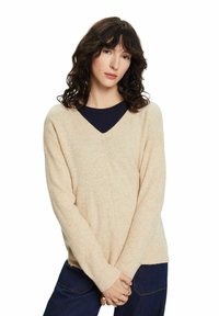 Beige v-hals trui met lange mouwen en een relaxte pasvorm. Zachte textuur met subtiele vlokken. Gelaagd over een donker shirt.