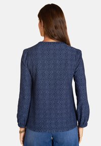 Navi blaue Bluse mit einem strukturierten Blumenmuster, langen puffärmel und einem runden Halsausschnitt. Der Stoff wirkt leicht und weich.