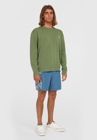 Groene sweatshirt met ronde hals, gemaakt van zachte stof, met ribbelmanchetten en -zoom. Gecombineerd met blauwe shorts met bloempatronen en witte sneakers.