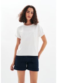 Top blanco de manga corta con puños enrollados, cuello redondo, textura suave, combinado con pantalones cortos azul marino oscuros con dobladillos doblados y bolsillos frontales.