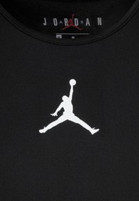 Czarna koszulka sportowa z wyraźnym białym logo "Jumpman" umieszczonym na środku z przodu. Materiał wydaje się gładki o dopasowanym kroju.