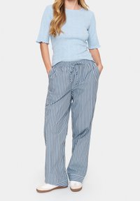 Ljusblå, figurnära stickad topp med korta, volangärmar, kombinerad med vida, randiga byxor i bl̊ått och grått. Vita skor.