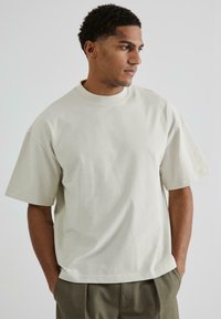 Light beige cotton t-shirt with a relaxed fit, short sleeves, and a round neck. Smooth texture, no visible patterns or hardware.