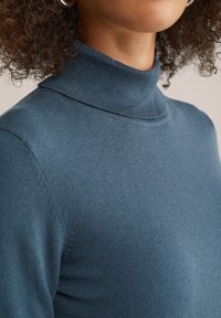 Pull col roulé bleu clair en tricot côtelé, présentant un design ajusté et une texture douce. La vue en gros plan met en avant les détails du col.
