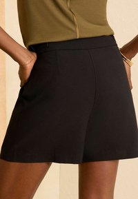 Mustad must shorts, mis on sileda tekstuuriga, küljetaskutega ja keskmise kõrgusega vöökohaga. Kangas näeb välja kerge ja kohandatud.