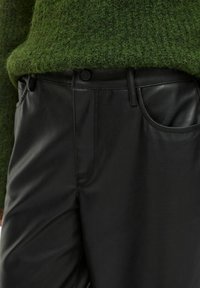 Černé kalhoty z umělé kůže s hladkým povrchem, které mají kapsy a pas zakončený knoflíkem. Hlava je z huňatého, zeleného úpletu.