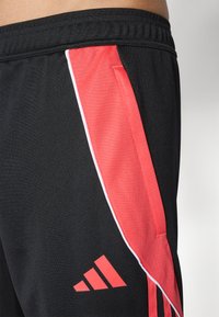 Black athletic pants with a red side stripe and white accents. Includes the Adidas logo on the lower leg. Smooth fabric texture.
