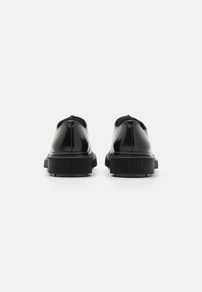 Black patent leather shoes with a rounded shape, smooth surface, and textured rubber sole. Features minimal stitching and a sleek design.