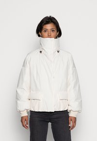 Veste blanche rembourrée à col montant, dotée de deux poches avant, d'une fermeture éclair et de poignets élastiques. Texture de tissu lisse.