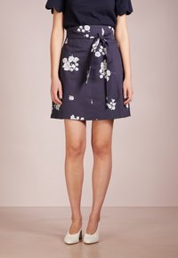 Laivari kukallinen hame, jossa on solmittava vyötärö ja valkoisia kukkapainatuksia. Kangas vaikuttaa sileältä ja kevyeltä, mikä tekee siitä sopivan lämpimille säille.