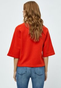 Maglietta rossa a maniche corte in maglia con una vestibilità ampia, caratterizzata da un orlo dritto e una texture semplice. Indossata con jeans in denim blu.