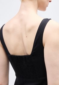 Κοντινό πλάνο του επάνω μέρους της πλάτης και των ώμων ενός ατόμου που φοράει μαύρο αμάνικο φόρεμα με ελαστική πιέτα.