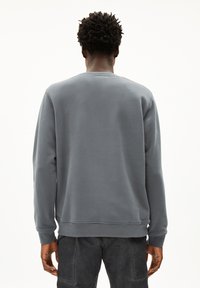 Sweatshirt gris à col rond fabriqué en tissu doux, avec des poignets et un bas côtelés. Design simple sans logos ni motifs visibles.