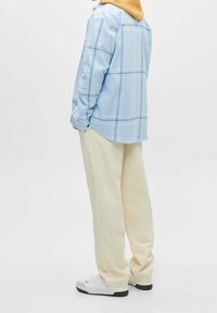 Camicia a quadri blu chiaro con maniche lunghe, pantaloni beige e sneaker bianche. La camicia presenta un motivo a quadri e una vestibilità comoda.