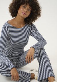 Mornarsko modra in bela črtasta majica z dolgimi rokavi in usklajene široke hlače, izdelane iz rebraste tkanine z valovitimi robovi, v kombinaciji z belimi športnimi copati.