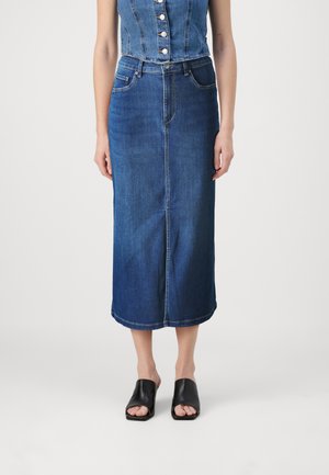 Denim midi skirt in dark blue with a fitted waist, five pockets, and subtle stitch detailing. Paired with black open-toe mules.