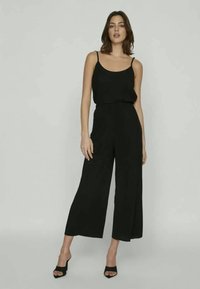 Fekete overál spagetti pántokkal, széles lábakkal és laza fazonnal. Simogató szövet, amely szépen redőzik, fekete tűsarokkal párosítva.