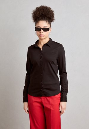 Zwarte overhem<Longsleeve> met knopen en een gladde textuur, gecombineerd met rode wijde broek. Accessoires zijn zwarte zonnebril.