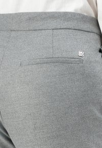 Pantalon gris taillé avec une texture lisse, doté d'une poche arrière et d'un petit logo en argent. Le design est classique et ajusté.
