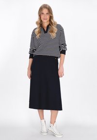 Marine gestreifter Strickpullover mit V-Ausschnitt, kombiniert mit einem einfarbigen marineblauen Midi-Rock und weißen High-Top-Sneakern. Lässige, entspannte Silhouette.