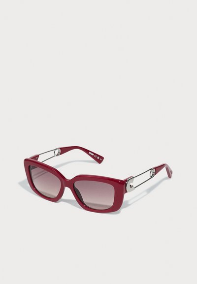 Óculos de sol retangulares oversized vermelhos com lentes degradê, armação em plástico brilhante e detalhes em metal prateado nas hastes.