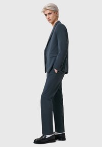 Mörkgrå kostym med en figursydd kavaj och raka byxor, gjord av ett mjukt material. Svarta loafers med silverdetaljer fulländar looken.