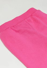 Detailní záběr na jasně růžové pletené legíny s elastickým pasem a shromážděným švy.