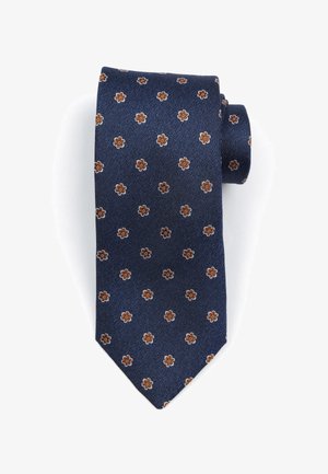 Donkerblauwe stropdas met een gestructureerde stof, voorzien van een klein bloemmotief in bruin en crème. Gevormd met een puntige tip en netjes opgerold.